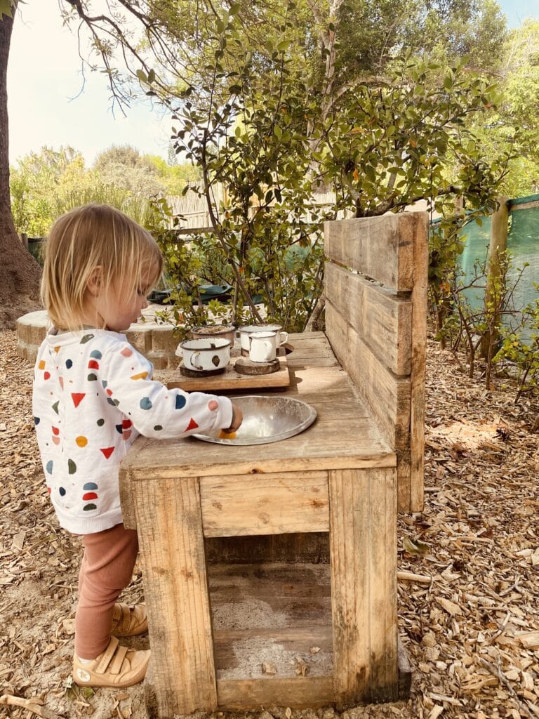 A child playing at the outdoor kitchen in a Waldorf environment.
