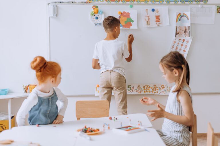 Children in classroom writing on whiteboard.