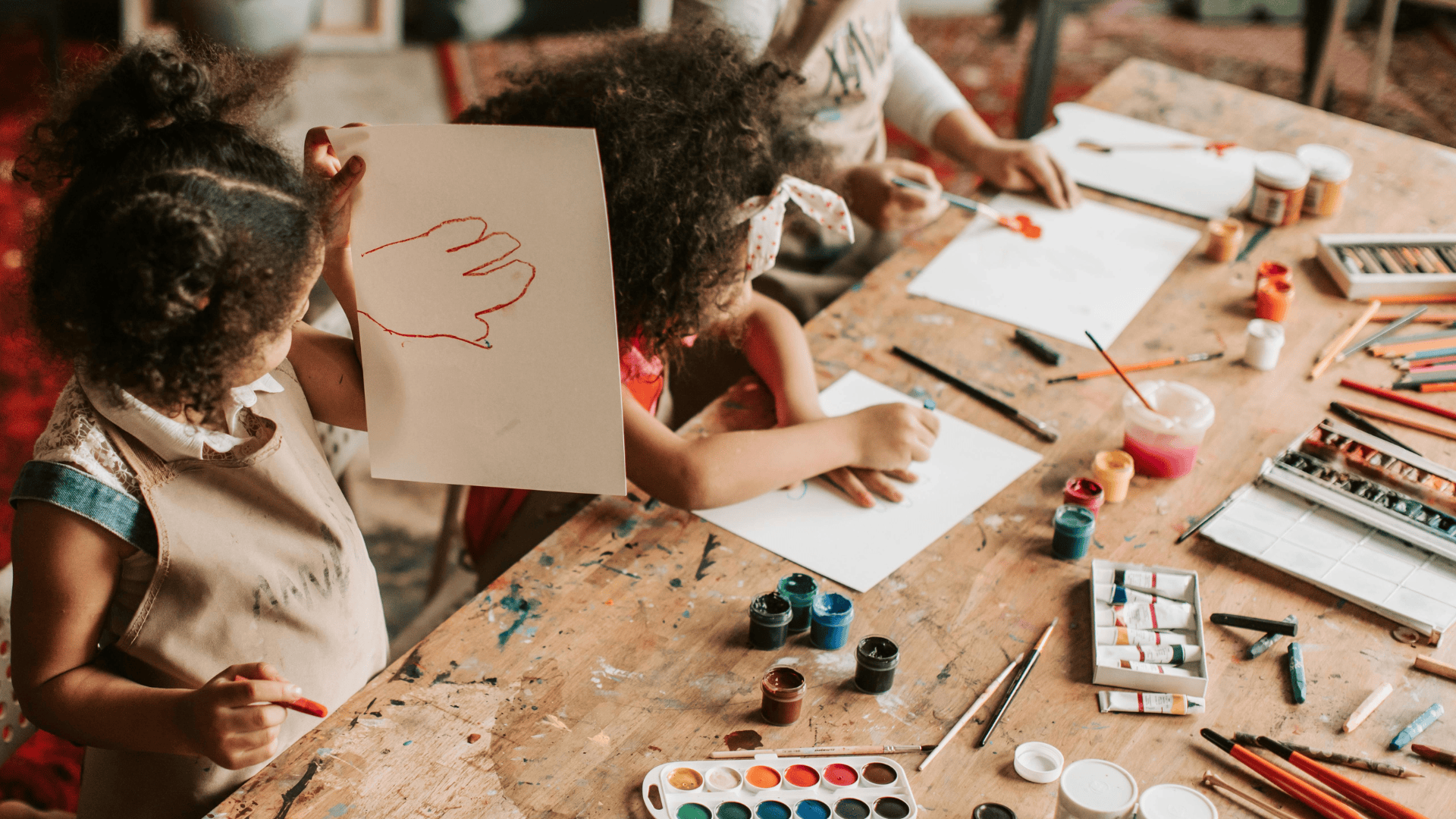 Children at a table in a preschool with paint and brushes.
